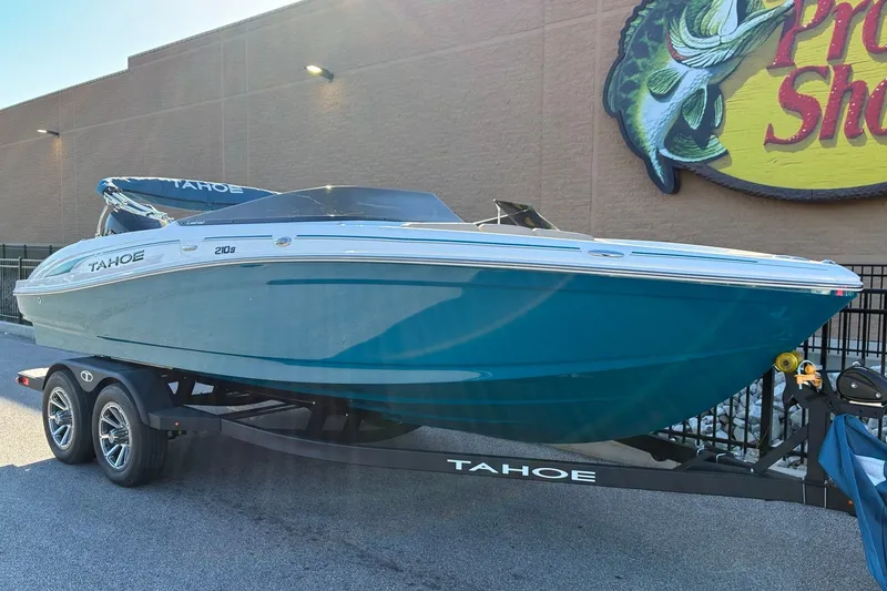 Slide: The Image of 2027 Tahoe 210 S boat on trailer, parked outside a store with a fish sign. - 6