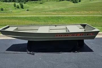 The Image of 2027 Tracker Grizzly 12 Jon boat on pavement, green landscape background. - 0