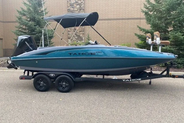 The Image of 2027 Tahoe 2150 boat on trailer, parked outdoors with trees and brick wall background. - 0
