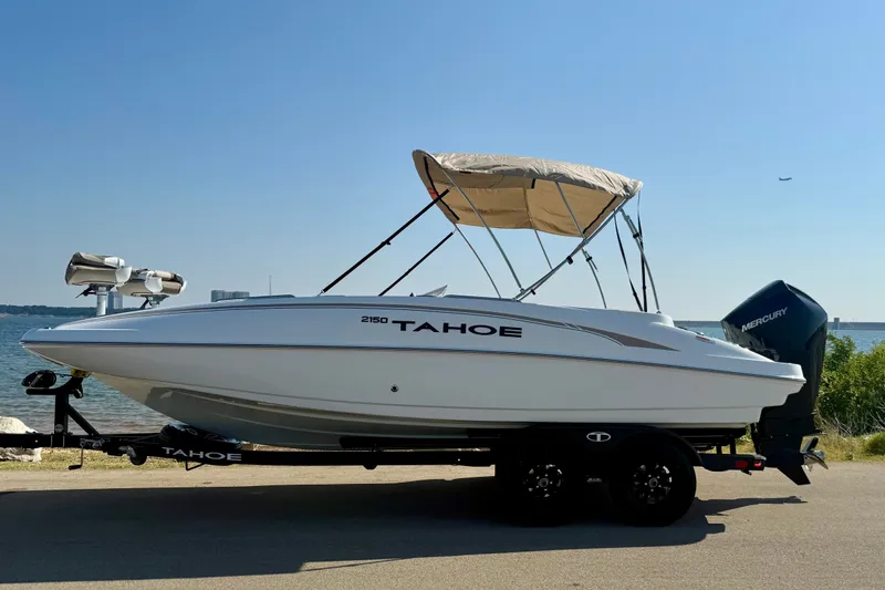 Slide: The Image of 2027 Tahoe 2150 boat with canopy, parked by a scenic waterfront. - 18