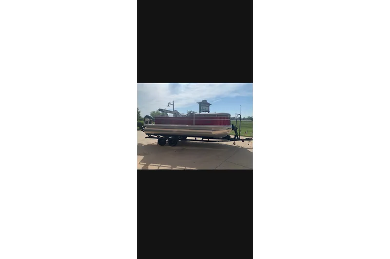 The Image of 2027 Sun Tracker SportFish 20 DLX pontoon boat on trailer, parked outdoors. - 0