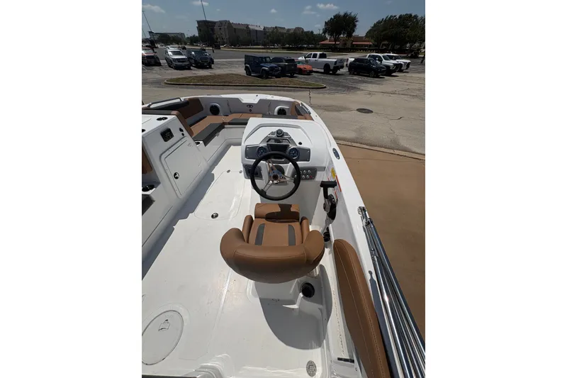 Slide: The Image of 2027 Tahoe 2150 boat interior with brown seating and steering wheel, parked outdoors. - 12