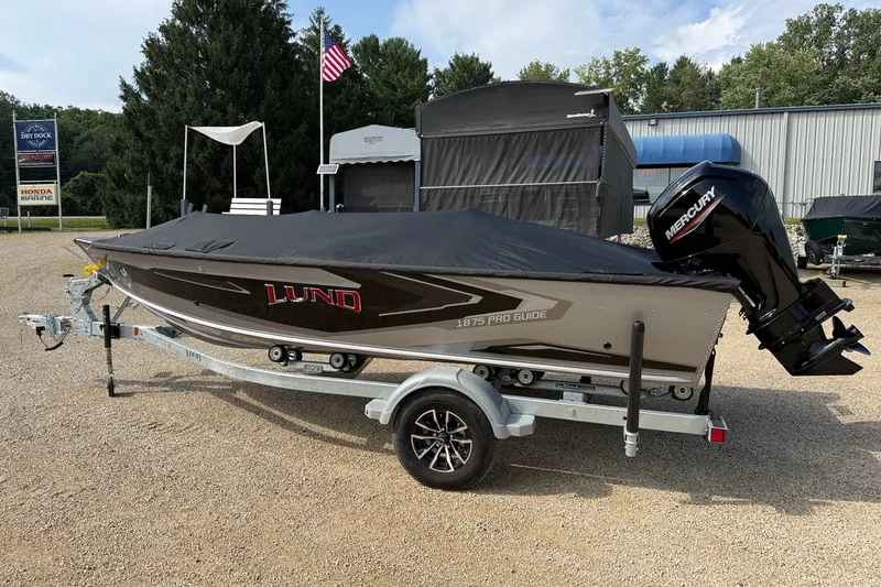 Slide: The Image of 2027 Lund 1875 Pro Guide boat with cover on trailer, parked outdoors. - 18