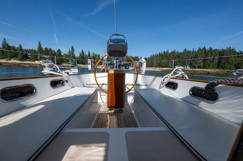 Slide: The Image of 1987 Hinckley Sou'wester 42 sailboat cockpit with wooden wheel, docked by a forested shoreline. - 24