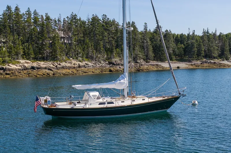 Slide: The Image of 1987 Hinckley Sou'wester 42 sailboat anchored in scenic coastal waters with forested shoreline. - 49
