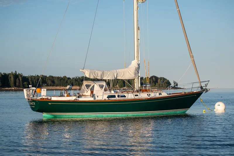 The Image of 1987 Hinckley Sou'wester 42 sailboat anchored on calm water, with forested shoreline in background. - 1