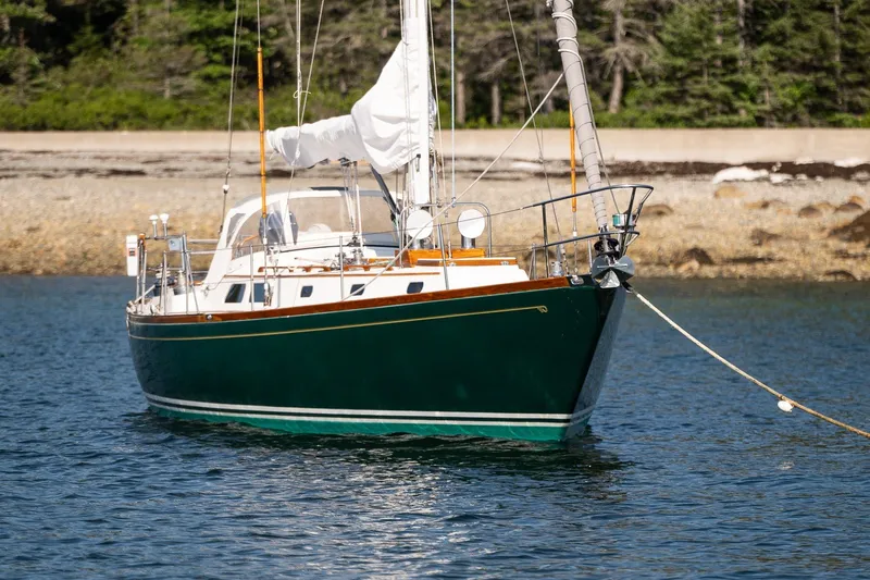 Slide: The Image of 1987 Hinckley Sou'wester 42 sailboat moored in calm waters near a rocky shoreline. - 3