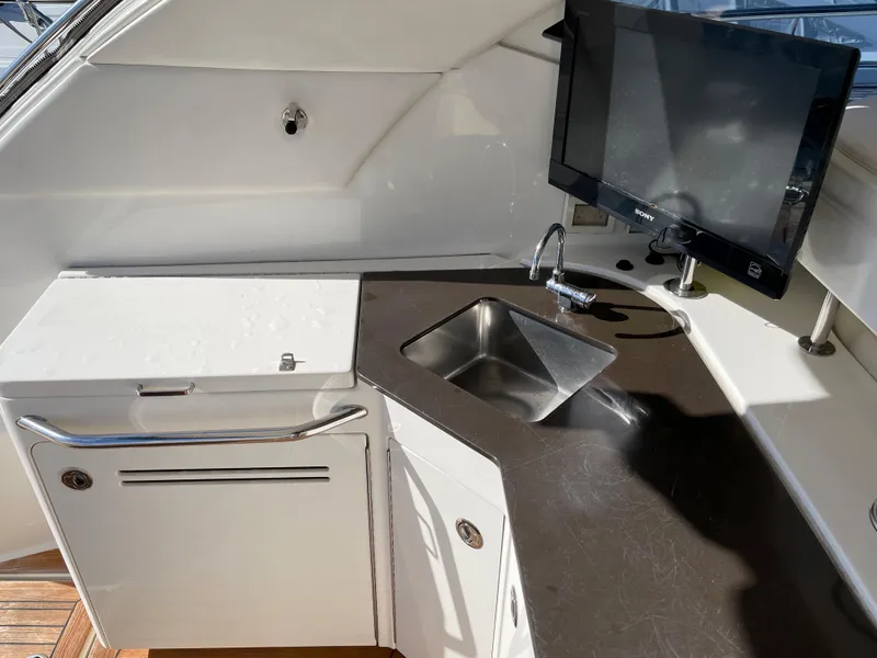 Slide: The Image of The 2012 Sea Ray 470 Sundancer features a modern kitchenette with a sink and flat-screen TV. - 13