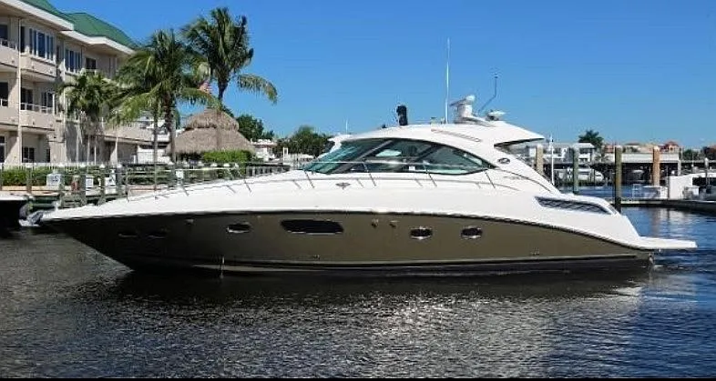 The Image of A 2012 Sea Ray 470 Sundancer is docked in the water near a marina with palm trees. - 0