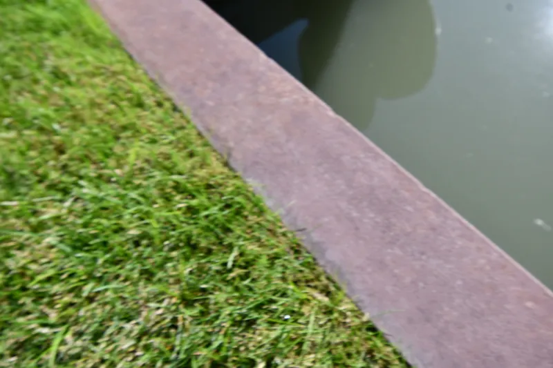 Slide: The Image of Grass and stone edge beside a calm water body. - 5