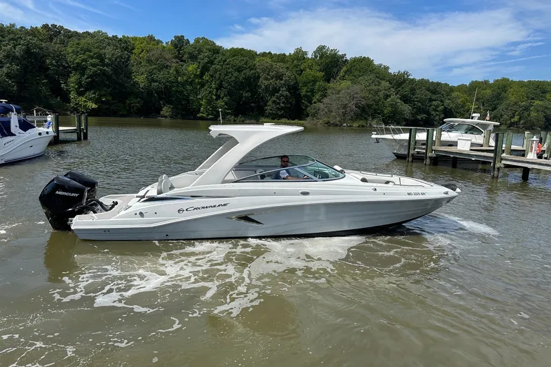 The Image of 2021 Crownline Eclipse E305 XS boat cruising on a scenic lake with lush greenery. - 0