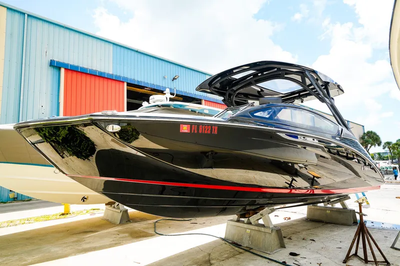The Image of 2025 Yamaha Boats 275SD in a marina, sleek black design, vibrant red stripe. - 0