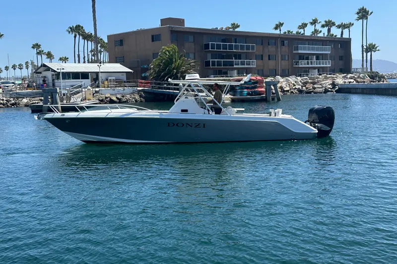 The Image of 2007 Donzi 35 ZF Cuddy boat docked in a marina with palm trees and buildings. - 0