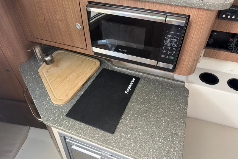 Slide: The Image of 2020 Boston Whaler 285 Conquest kitchen area with microwave, cutting board, and countertop. - 8