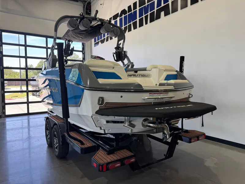 Slide: The Image of A 2020 Super Air Nautique G23 boat on a trailer in a showroom. It features a blue and white design. - 5