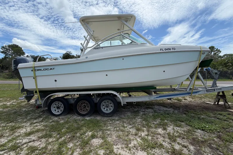 The Image of 2022 World Cat 230 DC boat on trailer, parked on grass under a partly cloudy sky. - 0