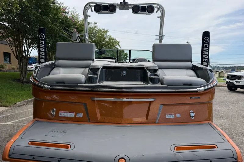 Slide: The Image of 2018 MasterCraft X26 boat with orange exterior and gray seating, parked outdoors. - 8