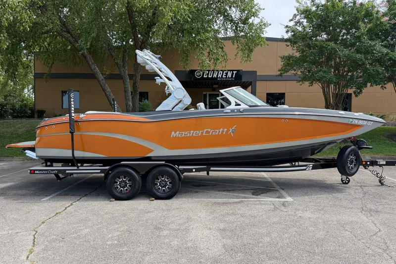 The Image of 2018 MasterCraft X26 boat in orange and gray on a trailer, parked outdoors. - 1