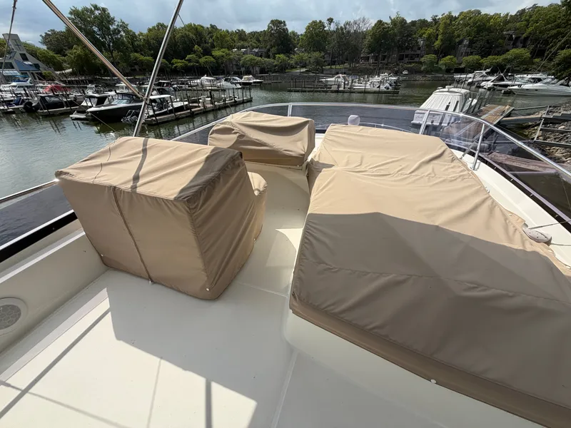 Slide: The Image of The 2015 Prestige 550 features a spacious flybridge with beige covers, overlooking a marina. - 47