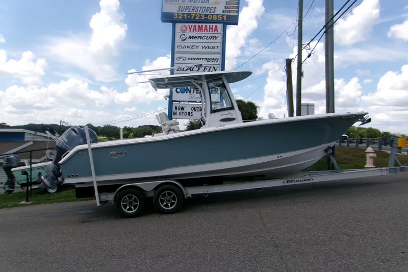 The Image of 2020 Sea Hunt Gamefish 25 boat on trailer, parked near dealership signs under a cloudy sky. - 0