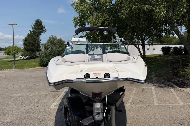 Slide: The Image of 2018 MasterCraft X46 boat on trailer in parking lot, surrounded by trees. - 1