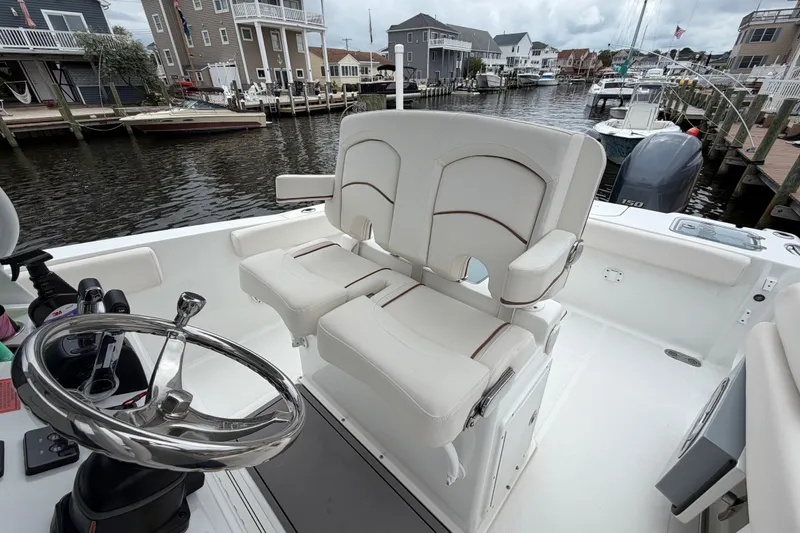 Slide: The Image of 2019 Sea Hunt Gamefish 25 boat interior with dual seats and steering wheel, docked in a marina. - 17