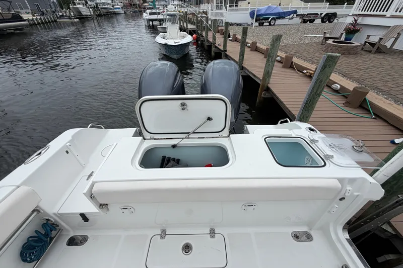 Slide: The Image of 2019 Sea Hunt Gamefish 25 boat docked, featuring open storage compartments and twin engines. - 13
