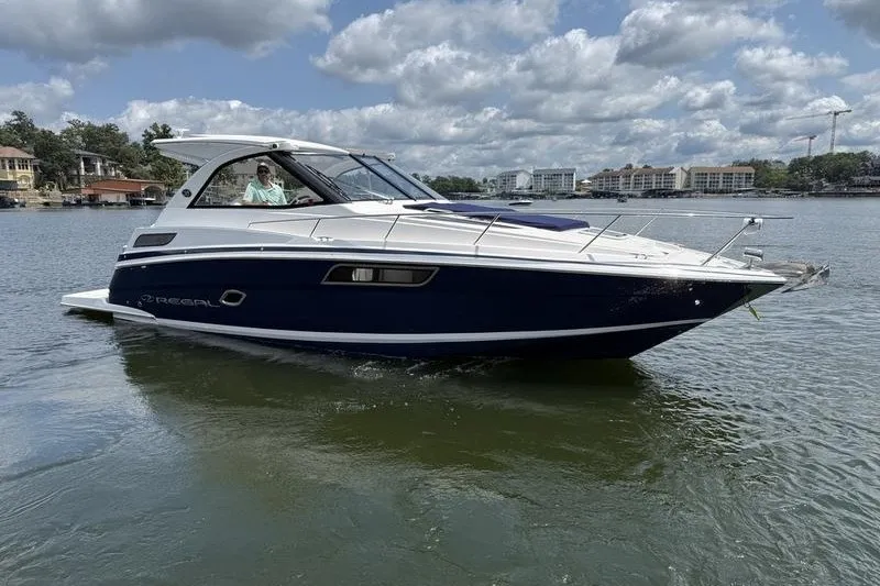 The Image of 2019 Regal 35 Sport Coupe boat cruising on a lake under a partly cloudy sky. - 1