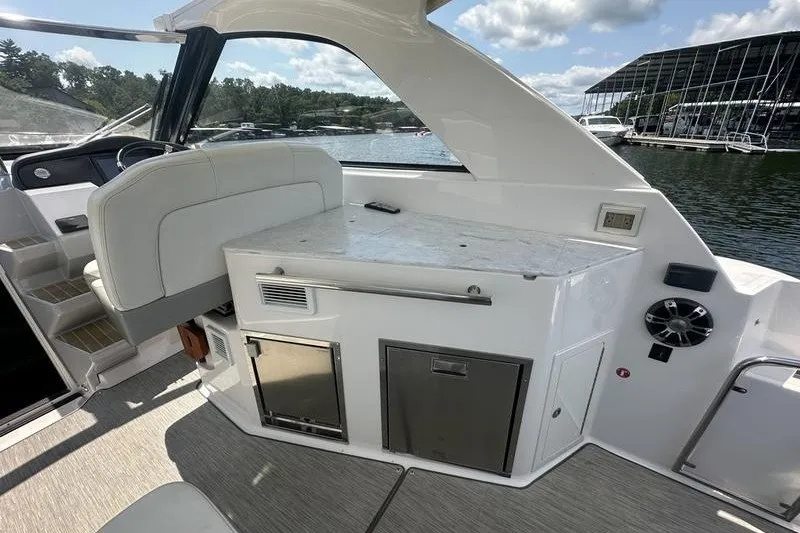 Slide: The Image of 2019 Regal 35 Sport Coupe interior with seating and kitchenette, docked by a lake. - 15