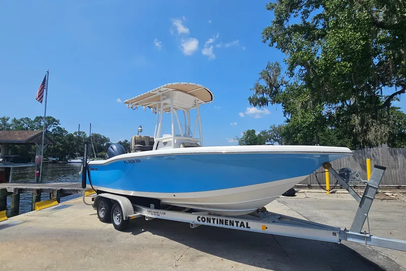 Slide: The Image of 2019 Tidewater 210 LXF boat on trailer, dockside with trees and American flag. - 4