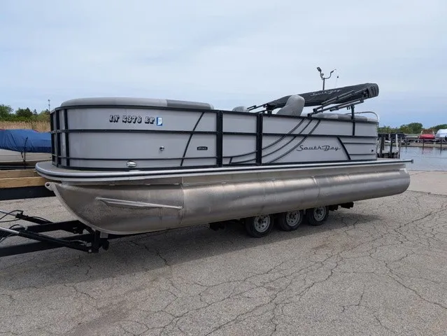 The Image of A gray South Bay pontoon boat, model S222RS 25", is on a trailer on land. - 1
