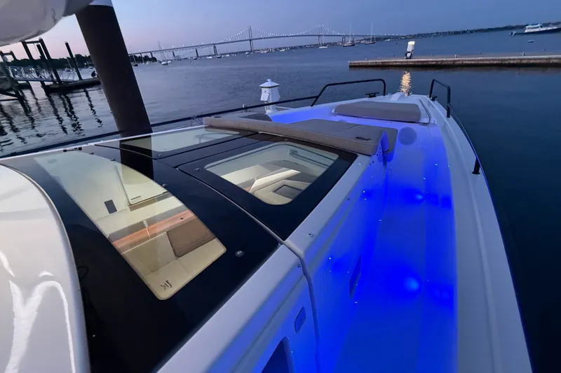Slide: The Image of 2024 Axopar 45 XC Cross Cabin boat with blue LED lights at dusk by the water. - 10