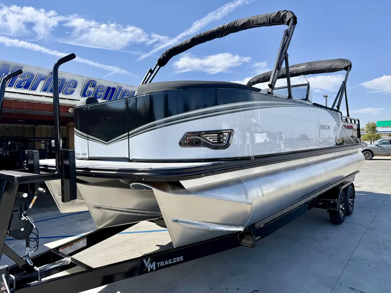 Slide: The Image of A modern Avalon pontoon boat with windshield, parked on a trailer outside a marine center. - 2