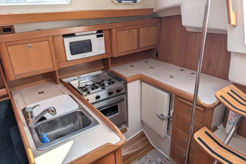 Slide: The Image of 2003 Catalina 350 yacht kitchen with stove, microwave, sink, and wooden cabinetry. - 23