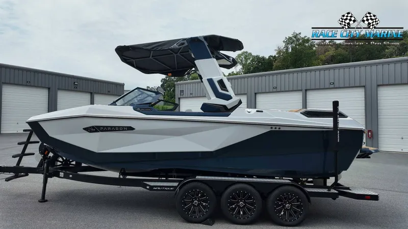 Slide: The Image of A modern Nautique P23 boat from 2027 on a trailer, parked in front of garage buildings. - 2