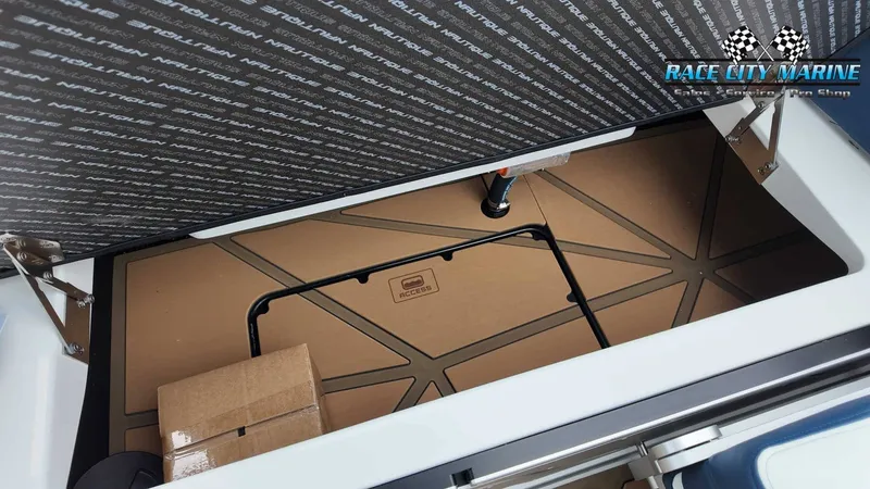 Slide: The Image of An open storage compartment on a 2027 Nautique P23 boat, with a cardboard box inside. - 28
