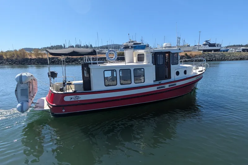Slide: The Image of 1997 Nordic Tug 32 boat with red hull cruising in a marina under clear blue skies. - 4