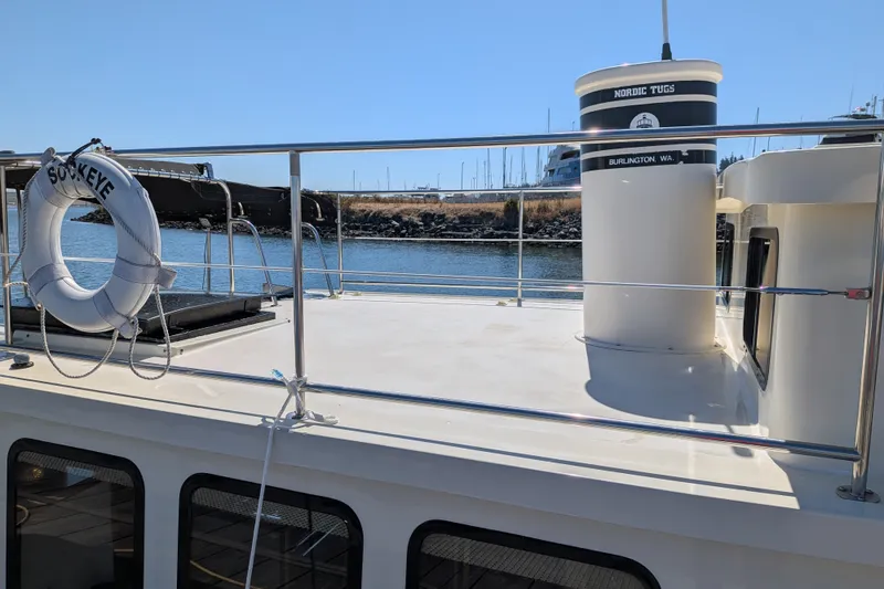 Slide: The Image of 1997 Nordic Tug 32 boat deck with railing and lifebuoy, docked by the water. - 12