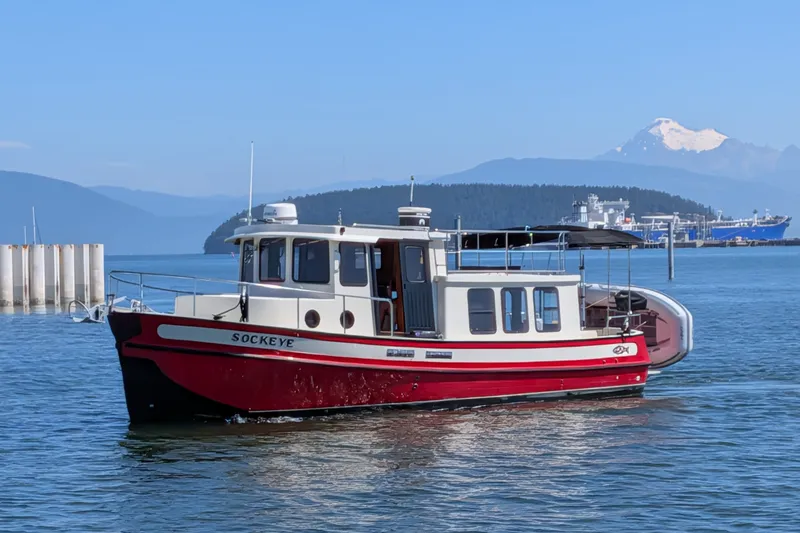 Slide: The Image of Red and white 1997 Nordic Tug 32 boat on calm water with mountains in background. - 51