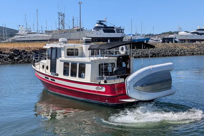 Slide: The Image of 1997 Nordic Tug 32 cruising in a marina, featuring a red and white design with a dinghy. - 1
