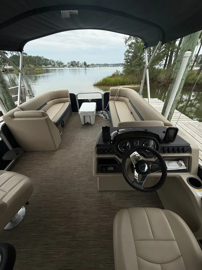 Slide: The Image of The image shows the interior of a Godfrey Sweetwater 2286 SFL pontoon boat. It features beige upholstered seating and a modern helm. A calm lake is visible in the background. - 9