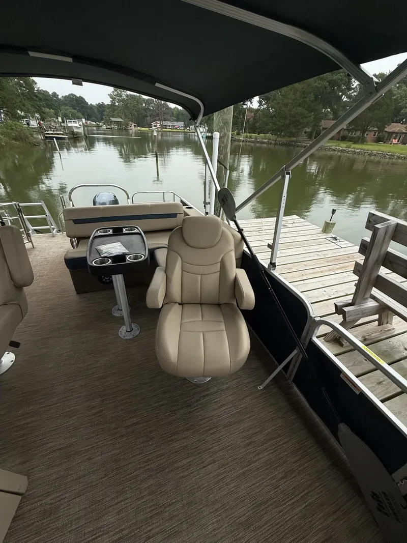 Slide: The Image of The image shows the cockpit of a 2022 Godfrey Sweetwater 2286 SFL. It features a beige captain's chair and helm. A calm river with a dock is visible in the background. - 14