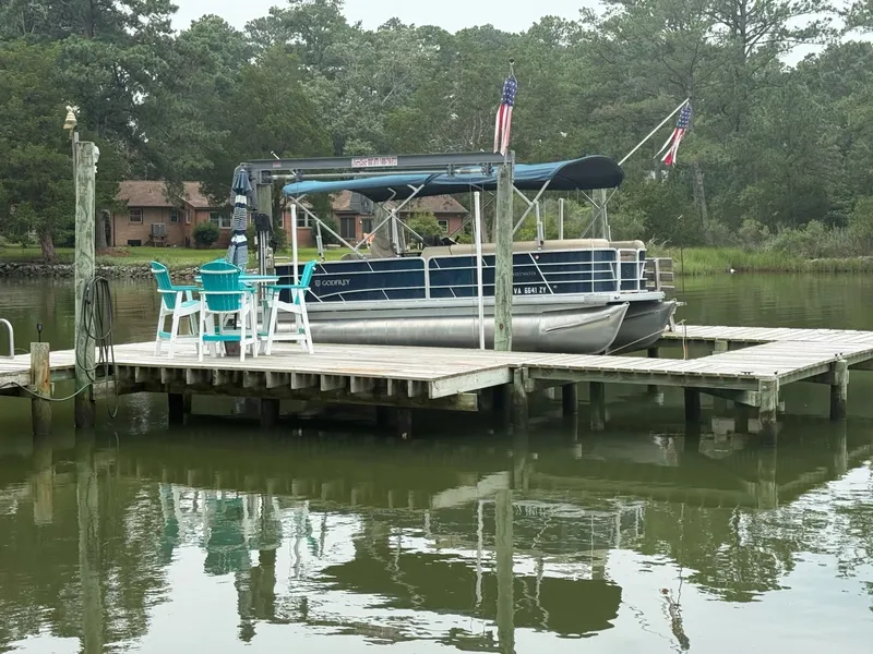 Slide: The Image of A 2022 Godfrey Sweetwater 2286 SFL pontoon boat docked at a serene pier with chairs. - 4