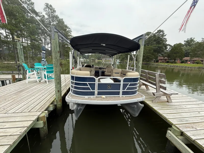 Slide: The Image of A 2022 Godfrey Sweetwater 2286 SFL pontoon boat docked at a wooden pier on calm water. - 2