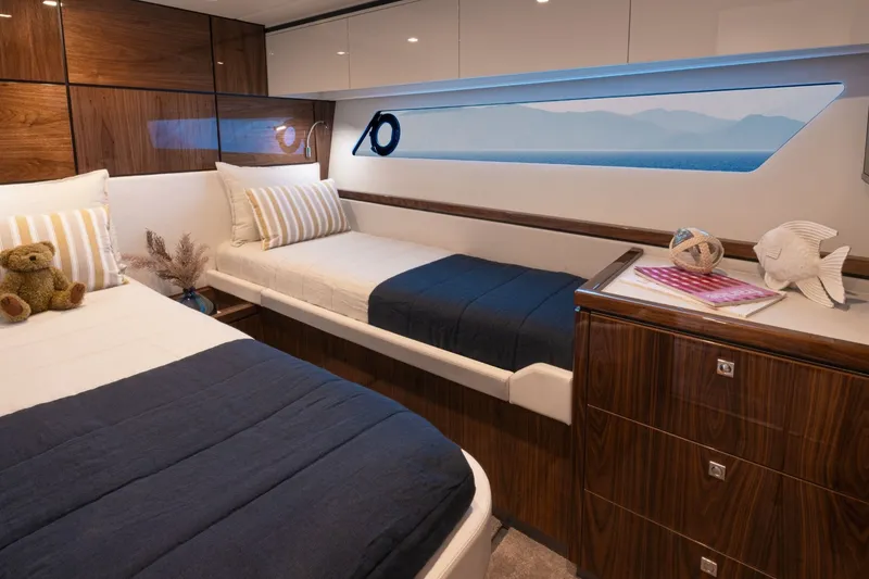 Slide: The Image of The cabin of the 2027 Riviera 5600 Sport Yacht Platinum Edition features two single beds with blue covers. - 18