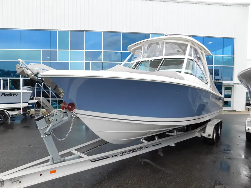 Slide: The Image of A 2023 Pursuit DC 246 Dual Console boat on a trailer in front of a modern building. - 2