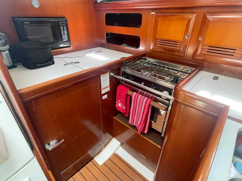 Slide: The Image of 2004 Beneteau 361 yacht kitchen with stove, microwave, and wooden cabinetry. - 42