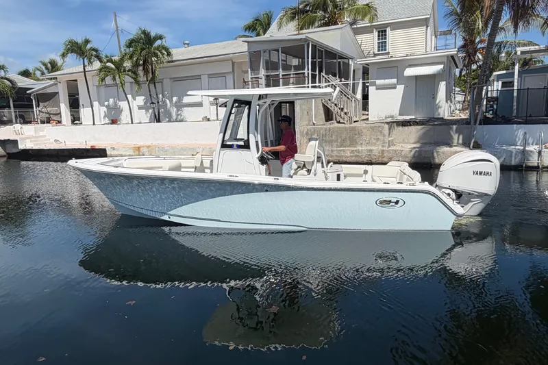 Slide: The Image of 2022 Sea Hunt Ultra 239SE boat on calm water near a dockside house. - 1