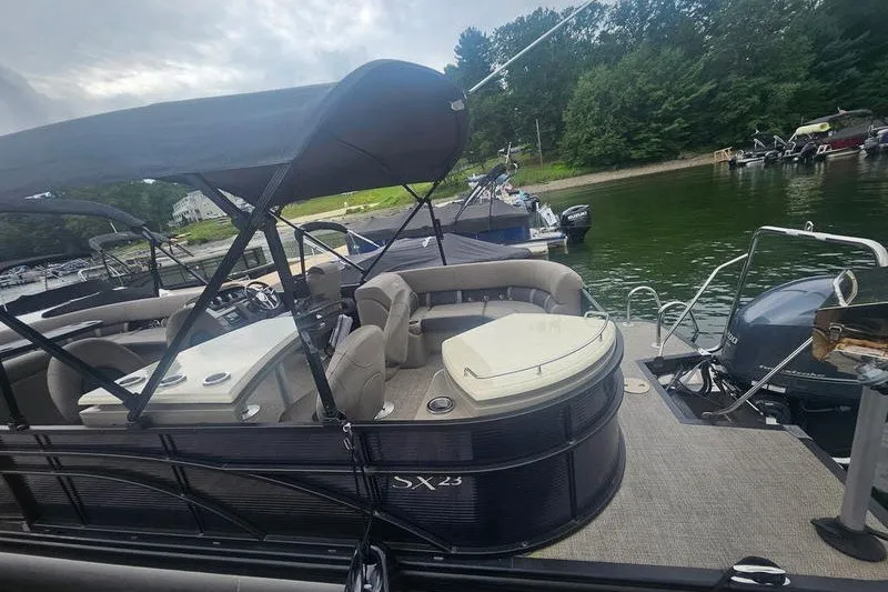 Slide: The Image of 2019 Bennington SX 23 SPDXP pontoon boat docked by a scenic lakeside. - 2