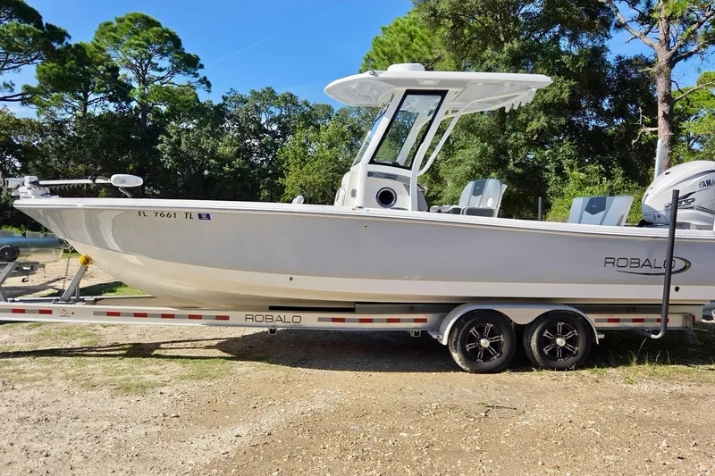 The Image of 2023 Robalo 266 Cayman boat on trailer, surrounded by trees and clear sky. - 0